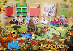 Dzieci siedzą na dywanie, jedna z dziewczynek układa jabłka.